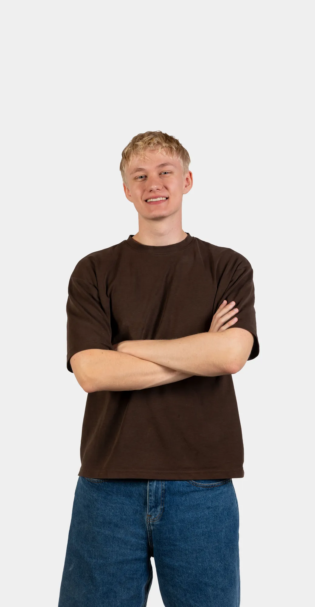 Anton Steffens står med armene over kors, iført en ensfarvet brun T-shirt og blå shorts foran en hvid baggrund.