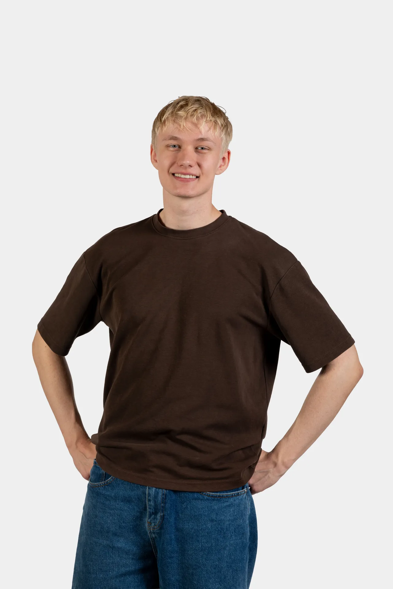 Anton Steffens står med hænderne i siden, iført en ensfarvet brun T-shirt og blå shorts foran en hvid baggrund.